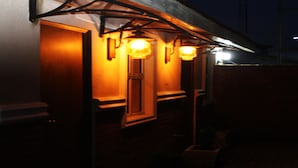 A building with a brick facade, a wooden door, and three illuminated wall sconces. - Fryburg Suites (Lagos)