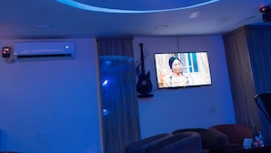 A modern living room with a TV, comfortable seating, and a unique ceiling design. - Fryburg Suites (Lagos)