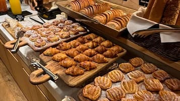 Un bufé con diversos pasteles y pan, incluyendo croissants y barras, exhibido sobre tablas de madera.