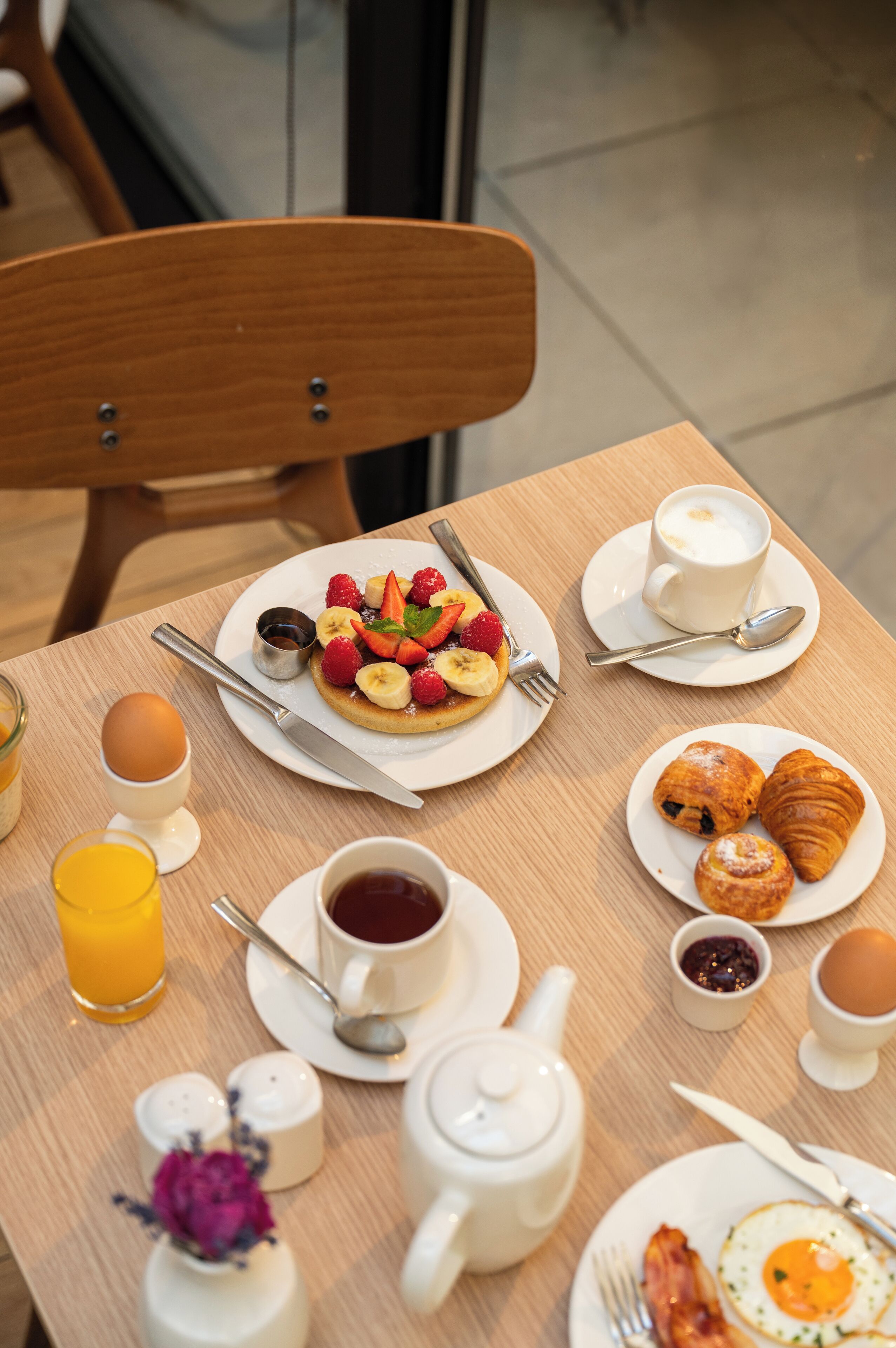 Une table de petit-déjeuner avec divers aliments, une théière, des tasses et des couverts.