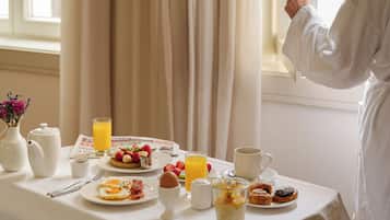 A breakfast table with various food items and a person opening a window blind.