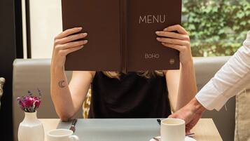 Iemand houdt een menu vast aan een tafel, met een kopje en schotel, een vaas met bloemen, en een vork en lepel op een servet.