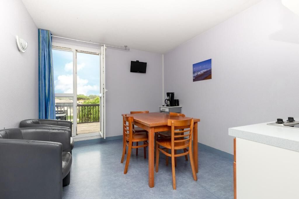 A room with a dining table, chairs, a sofa, a kitchen area, and a balcony with a view.
