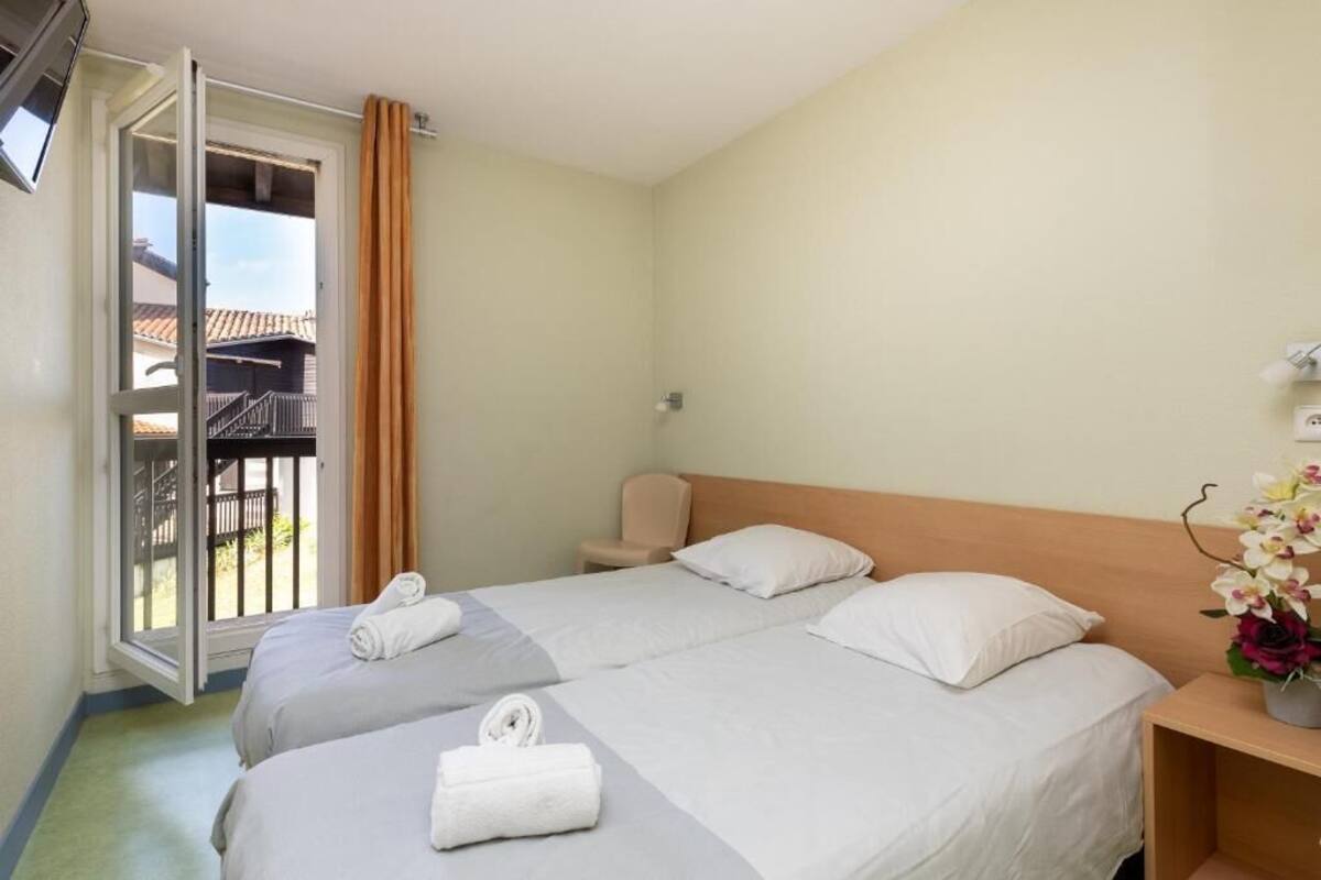 A hotel room with two beds, a balcony, and a small table with a vase of flowers.