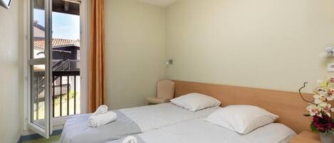 A hotel room with two beds, a balcony, and a small table with a vase of flowers.