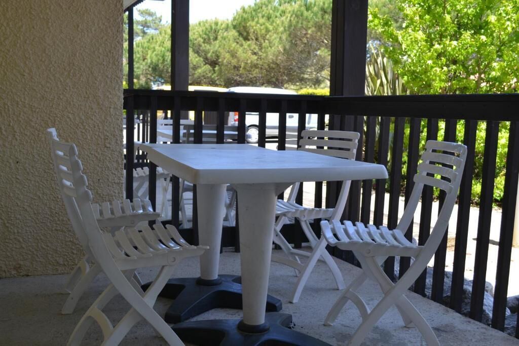 Une table et des chaises en plastique blanc sur un balcon doté d’une rambarde noire.