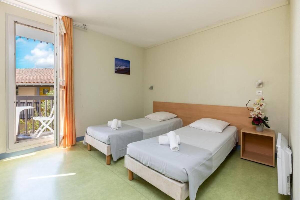 A hotel room with two beds, a balcony, a small table with a vase of flowers, and a painting on the wall.