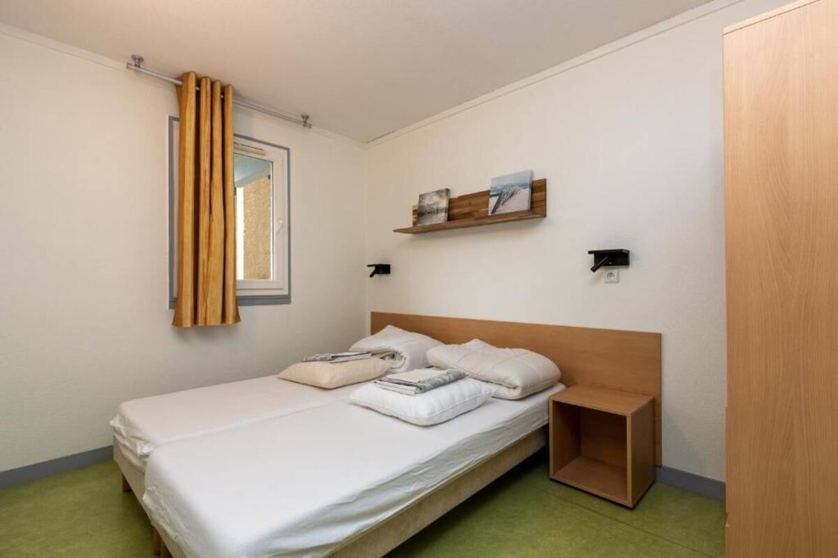 A single bed with a wooden headboard, a bedside table, and a small shelf with pictures.