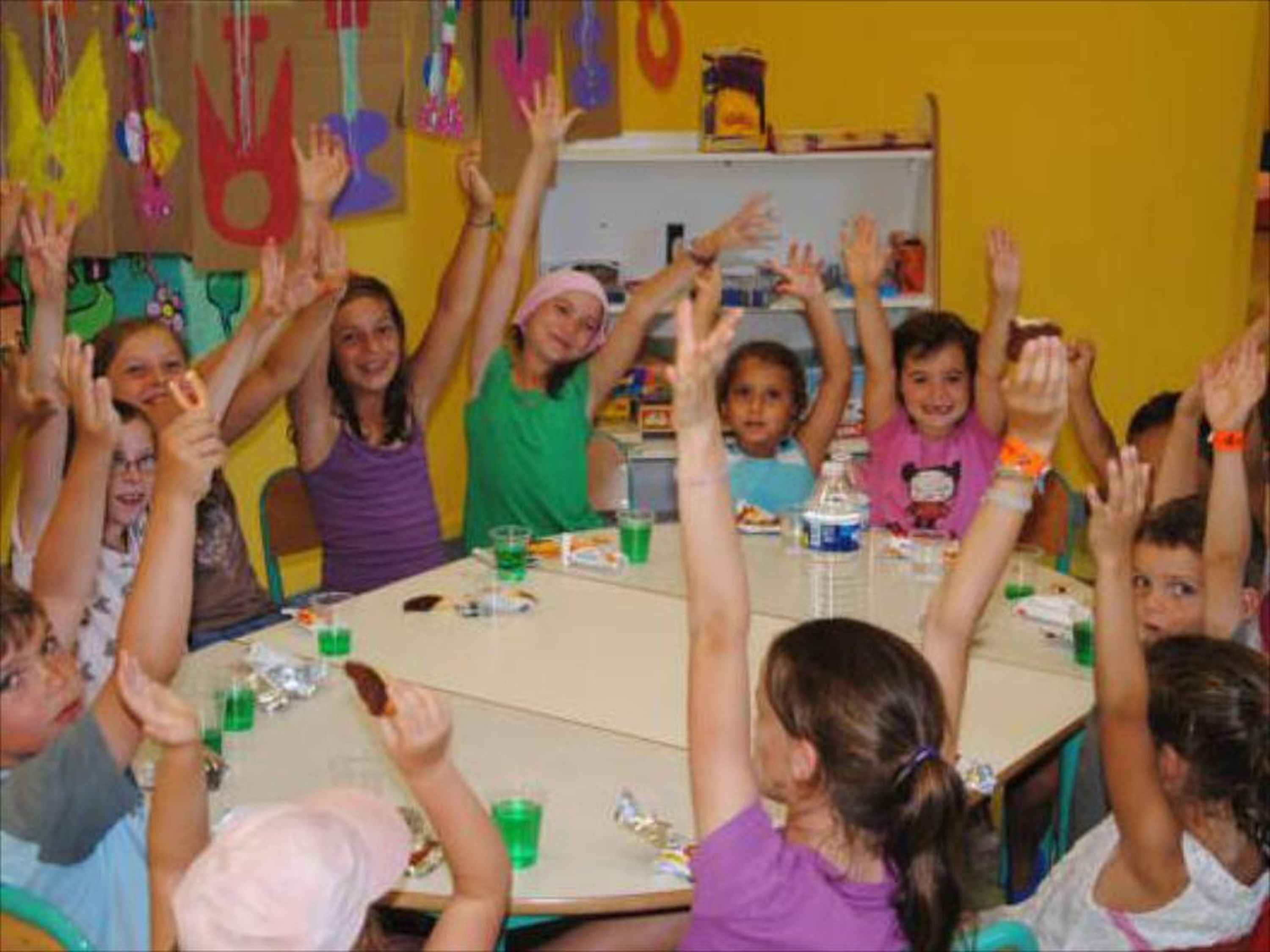 Un groupe d’enfants assis autour d’une table, les mains levées, probablement dans une salle de classe ou lors d’une réunion.