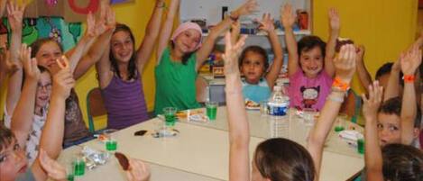 Un groupe d’enfants assis autour d’une table, les mains levées, probablement dans une salle de classe ou lors d’une réunion.