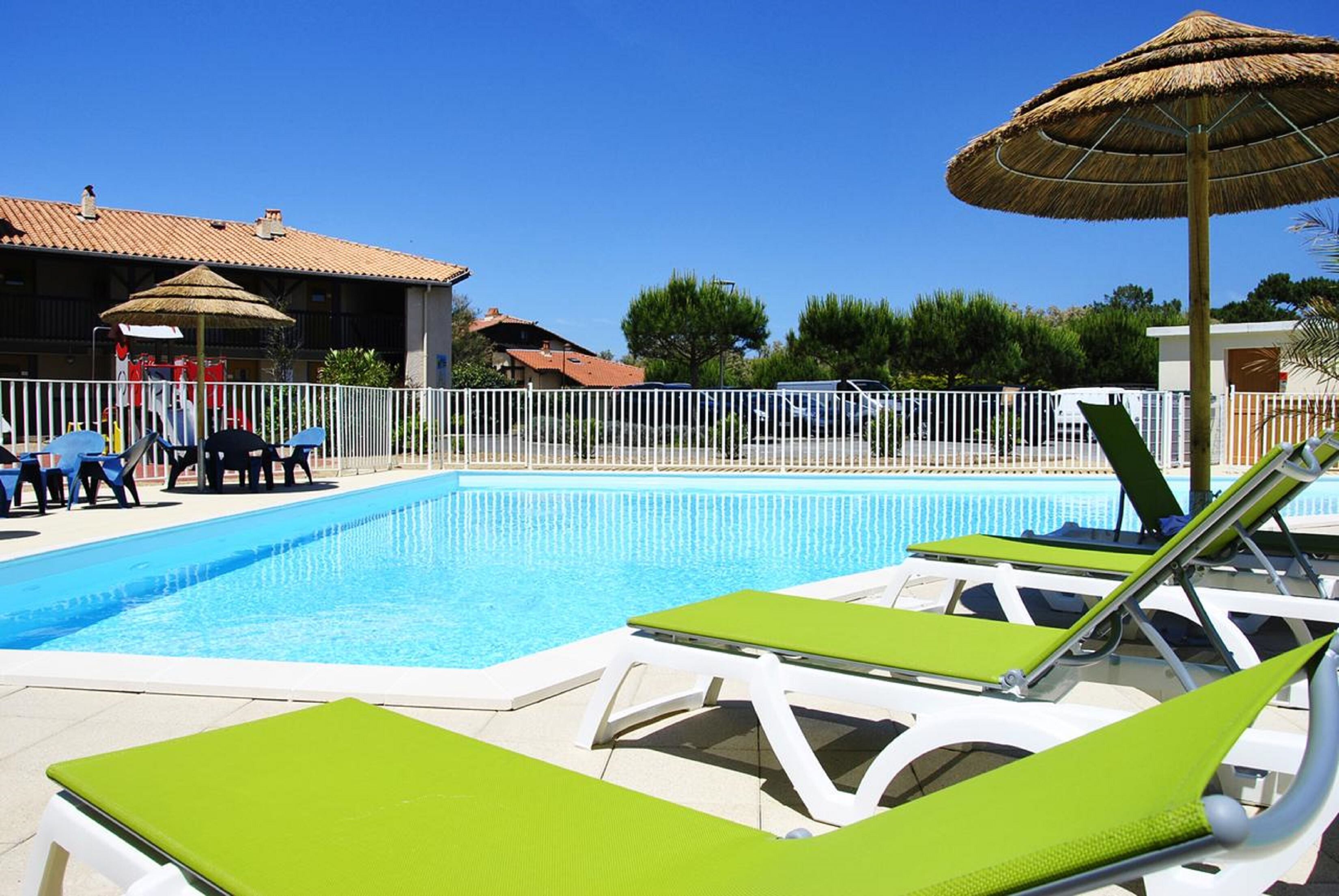 A swimming pool with lounge chairs and umbrellas, surrounded by a white fence.