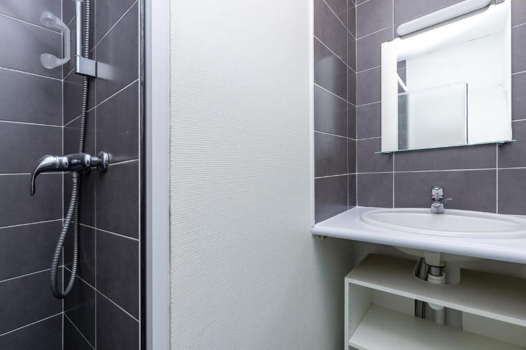 A bathroom with dark tiles, a shower, a sink, and a mirror.