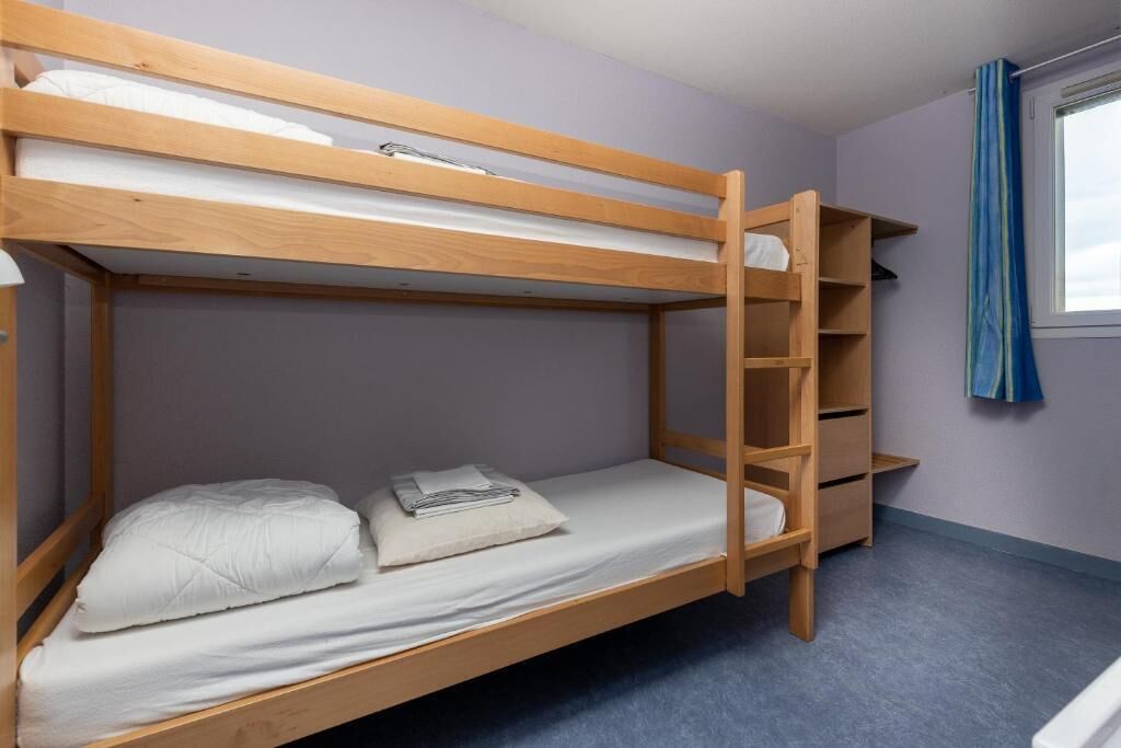 A bunk bed with a wooden ladder, a small shelf, and a window with a curtain.