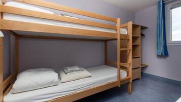 Una cama litera con una escalera de madera, un estante pequeño y una ventana con cortina.