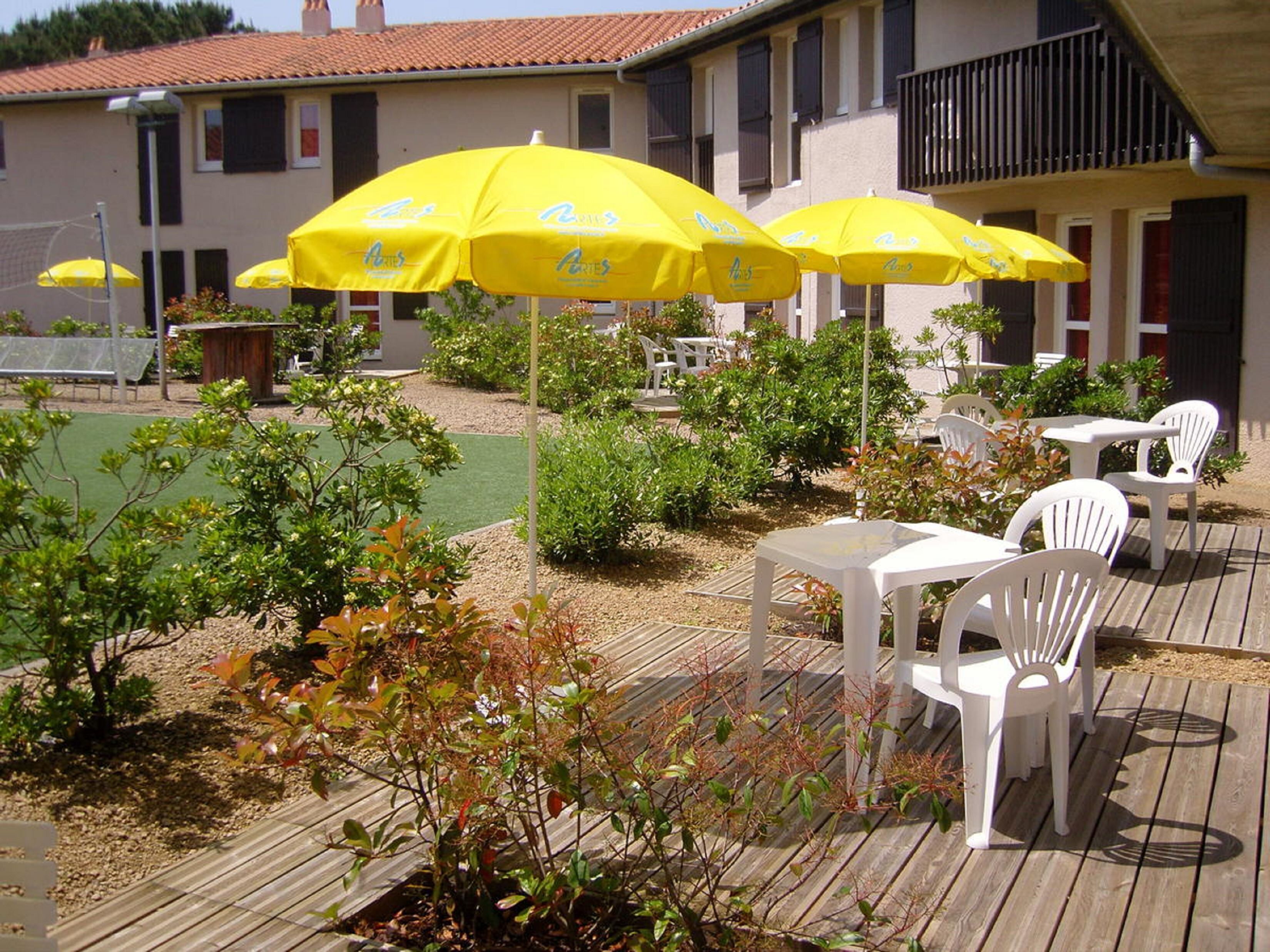 An outdoor patio area with yellow umbrellas, white plastic chairs, and a wooden deck.