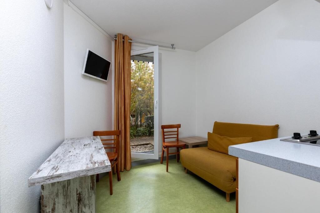 A compact room with a kitchenette, a sofa, a dining table with chairs, and a TV mounted on the wall.