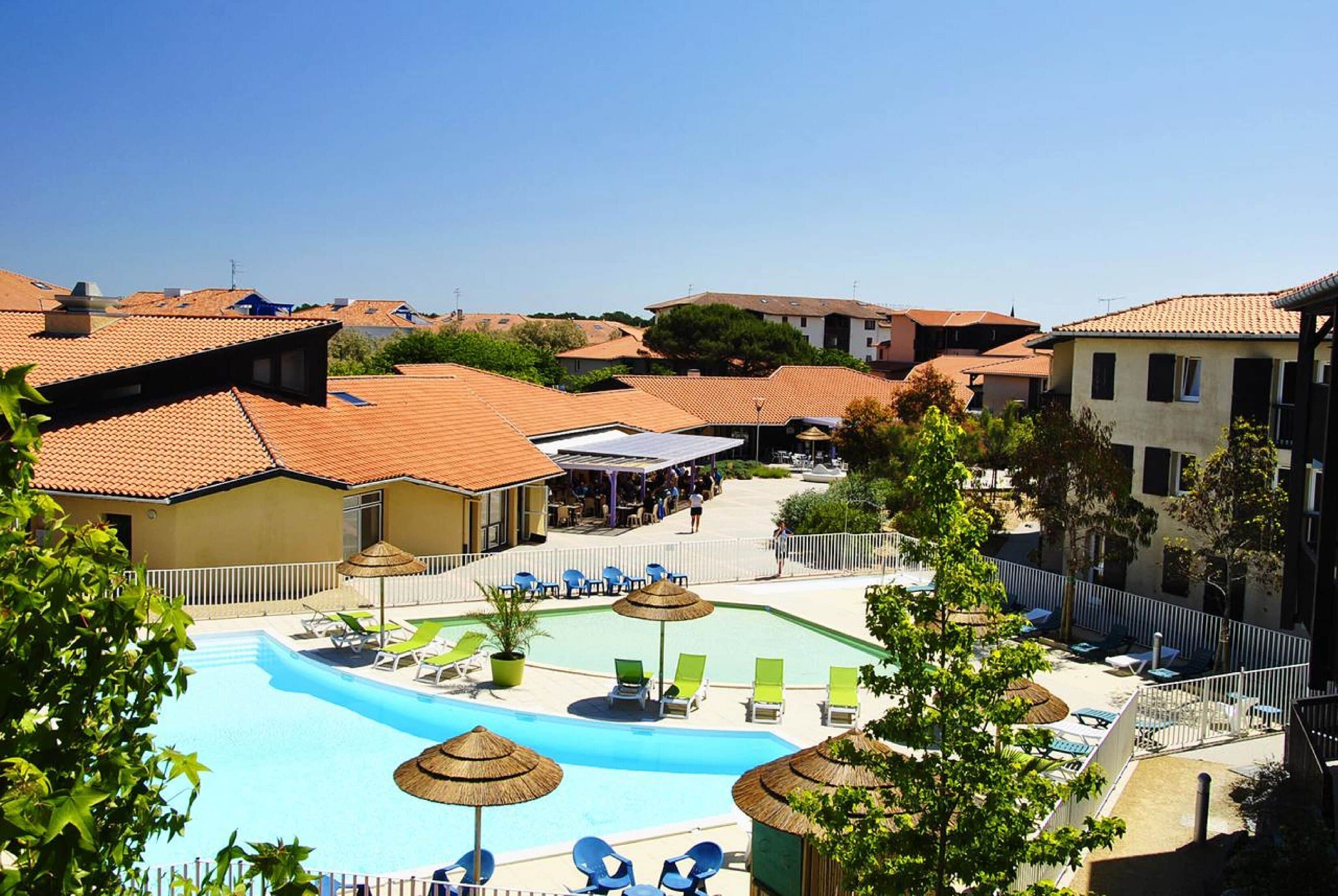 A rooftop swimming pool with lounge chairs and umbrellas, surrounded by residential buildings.