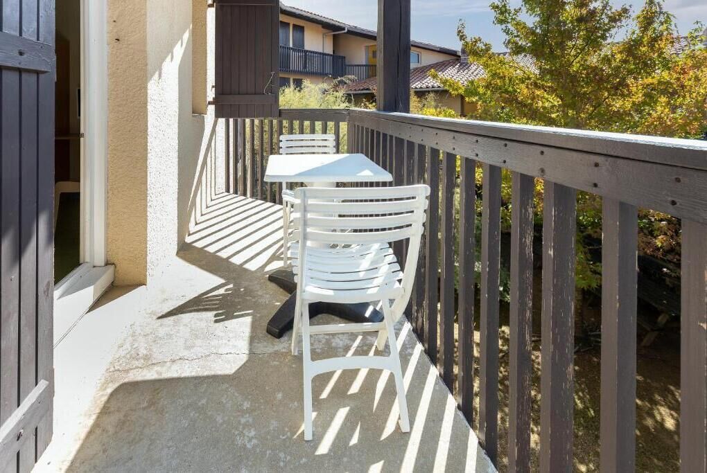 A balcony with a white table and chairs, a wooden railing, and a view of buildings and trees.