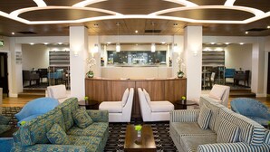 Een moderne lobby met een centraal receptiebalie, een zithoek met gestreepe banken en een vloer met een patroon.