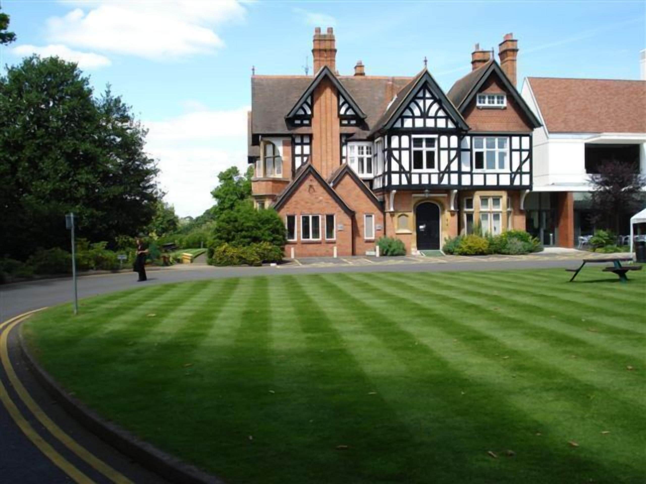 A large, traditional building with a symmetrical facade, multiple chimneys, and a well-maintained lawn in front.