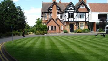 A large, traditional building with a symmetrical facade, multiple chimneys, and a well-maintained lawn in front.