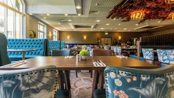 A restaurant with blue upholstered booths, wooden tables, and patterned chairs.