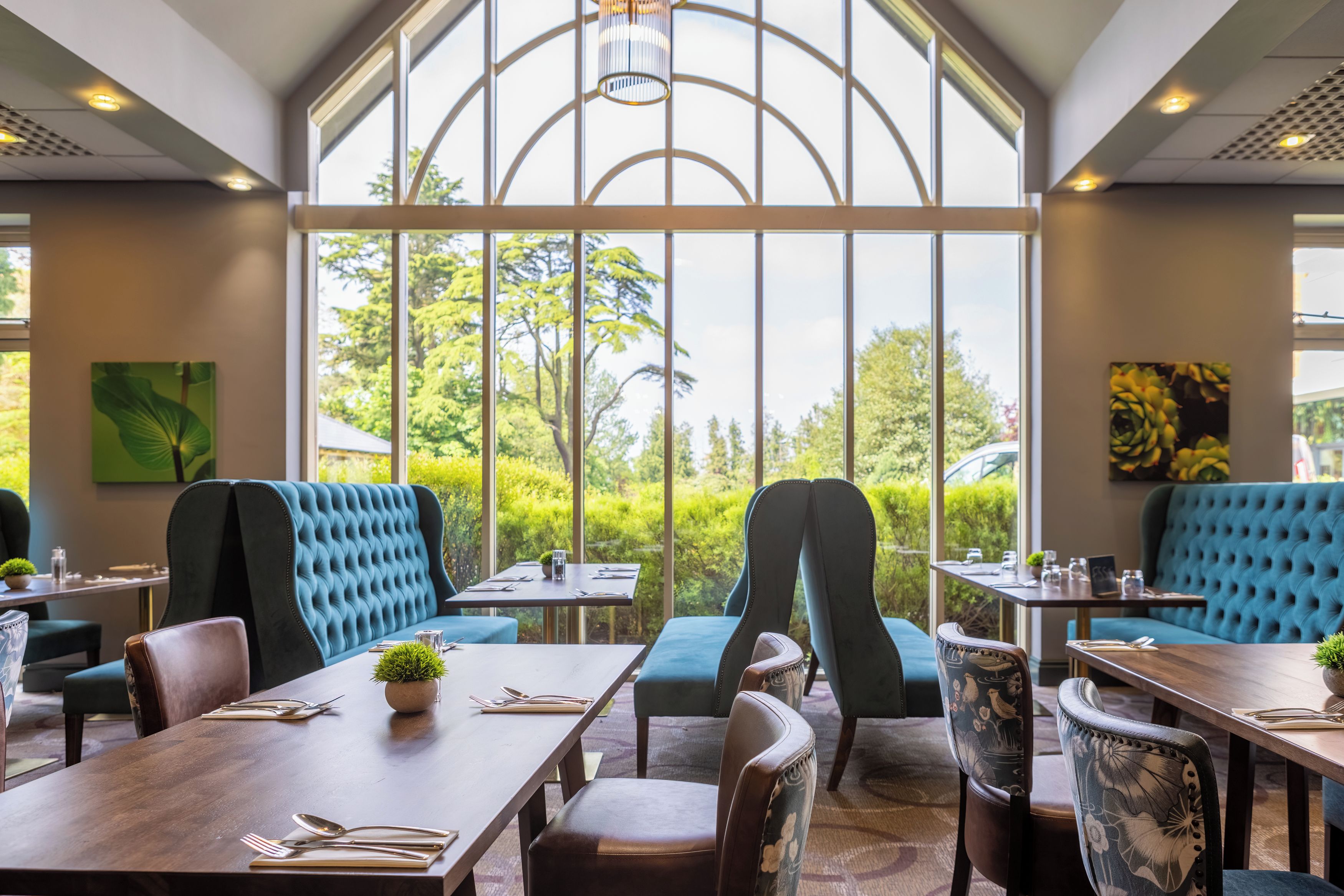A restaurant with high ceilings, large windows, and a view of greenery.