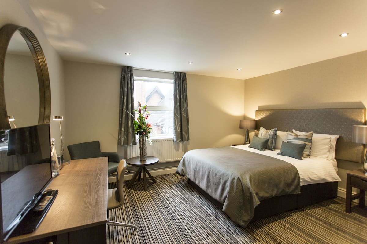 Een hotelkamer met een bed, nachtkastje, stoel, bureau, televisie en een raam met gordijnen.