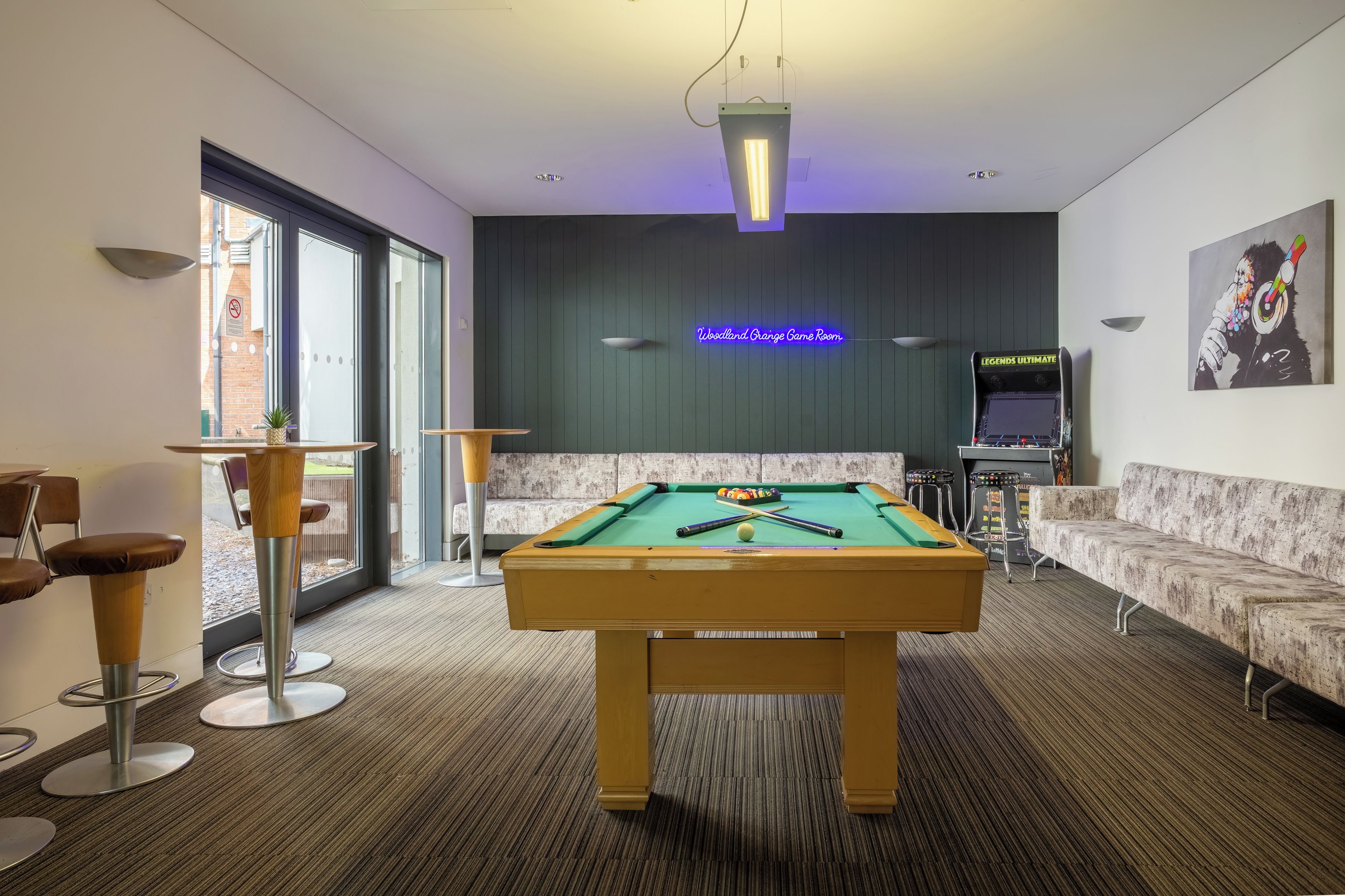 A pool table in a room with a neon sign, a sofa, and a bar area.