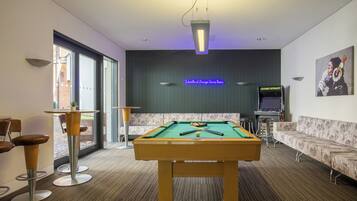A pool table in a room with a neon sign, a sofa, and a bar area.