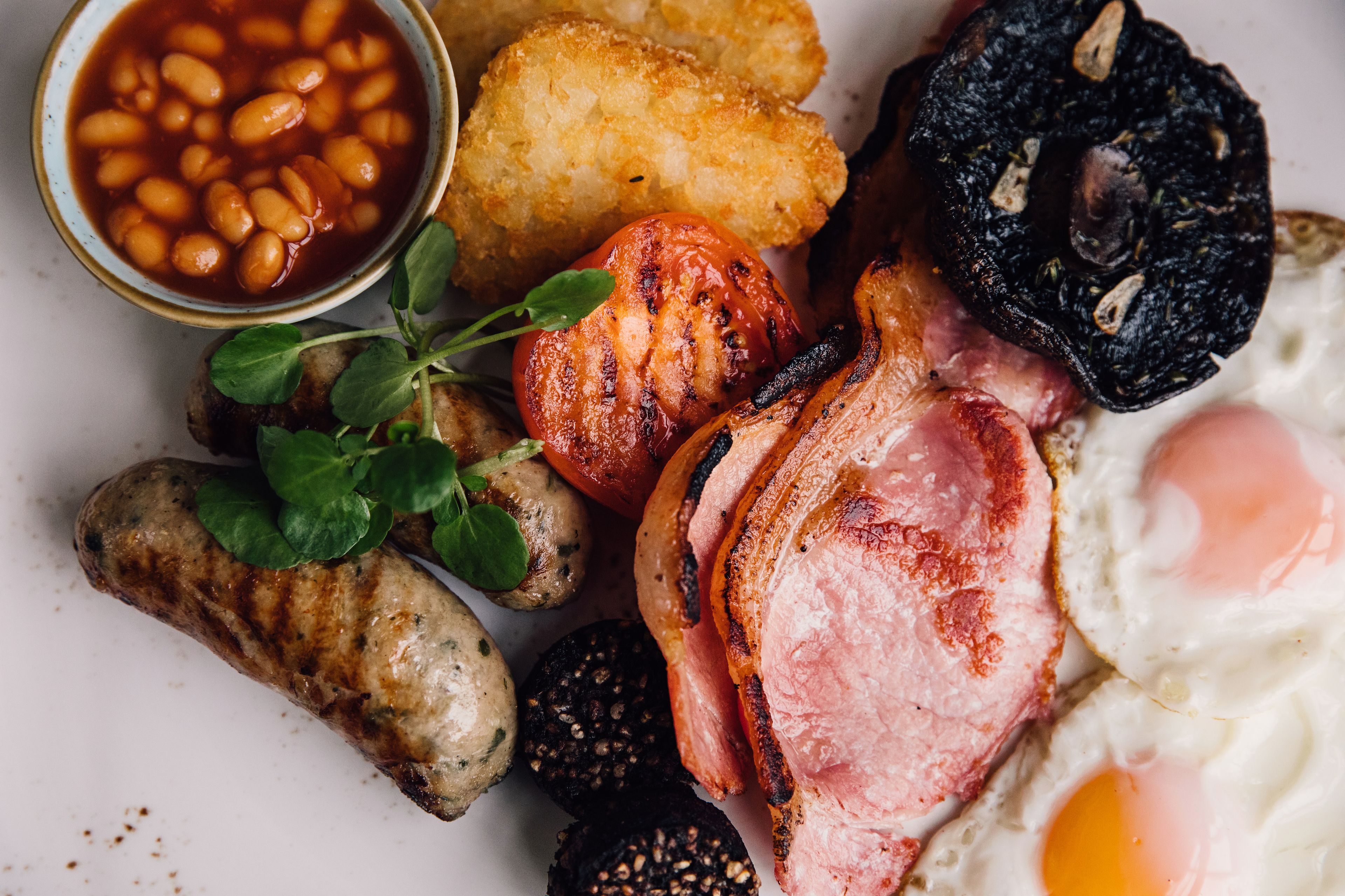 A breakfast plate with various items including beans, sausage, bacon, an egg, and mushrooms.