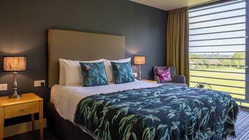 Een hotelkamer met een bed, twee nachtkastjes, een lamp, een stoel en een raam met jaloezieën.