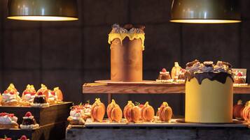 Mostra de postres amb diferents pastissos i un pastís gran, il·luminat per llums del sostre.