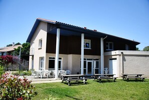 Um edifício de dois andares com telhado plano, janelas amplas e varanda coberta com área para sentar ao ar livre.