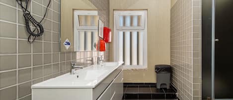 A compact bathroom with a white sink, a mirror, a hairdryer, and a trash bin.