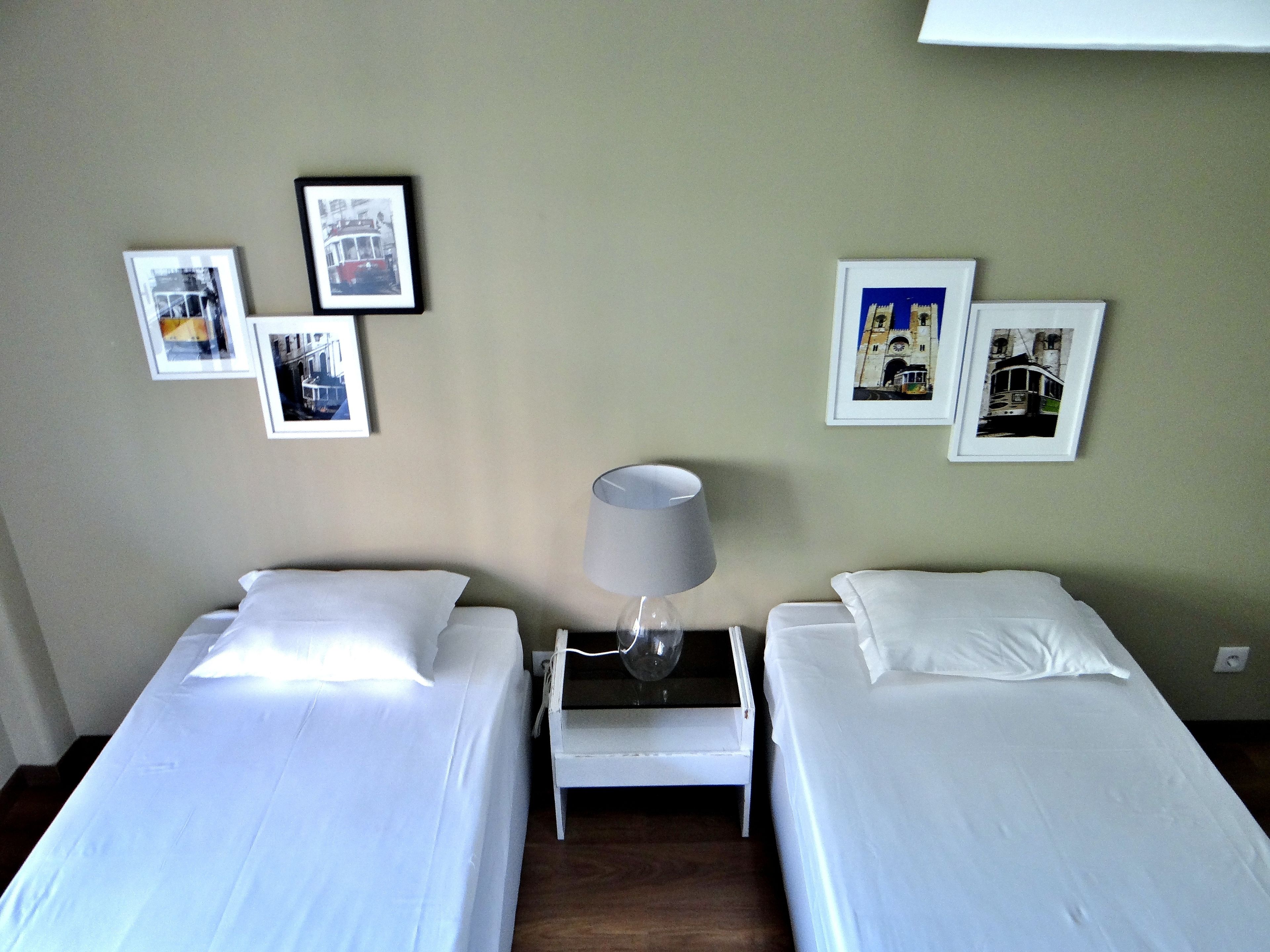 Una habitación de hotel con dos camas individuales, una mesita de noche con lámpara y tres cuadros enmarcados en la pared.