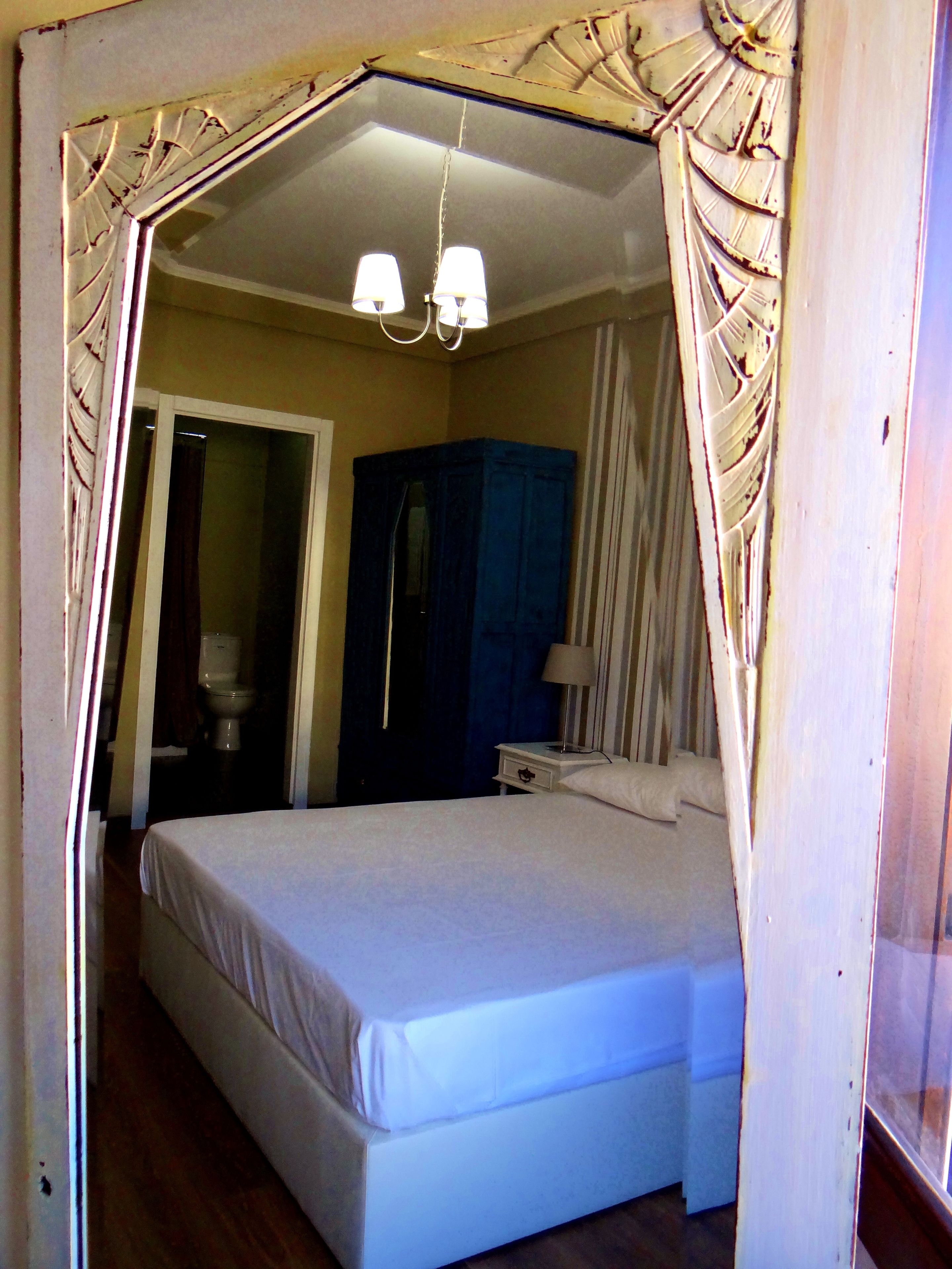 Ein Schlafzimmer mit Bett, Nachttisch, Kommode, Spiegel und einer Tür zum Badezimmer.