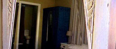 Une chambre à coucher comprenant un lit, une table de chevet, une commode, un miroir et une porte donnant sur une salle de bain.