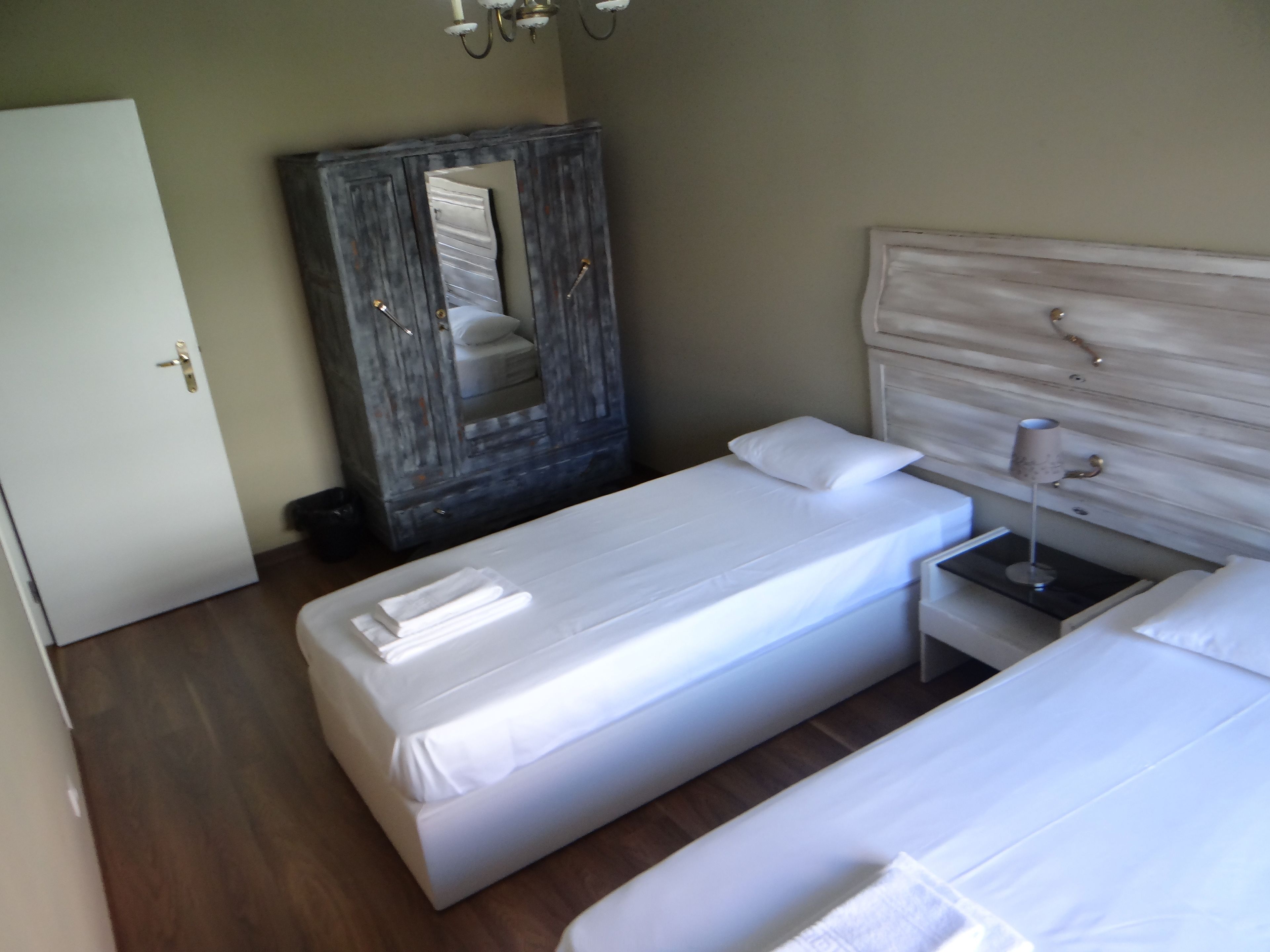 A hotel room with two beds, a wardrobe, a bedside table with a lamp, and a door.