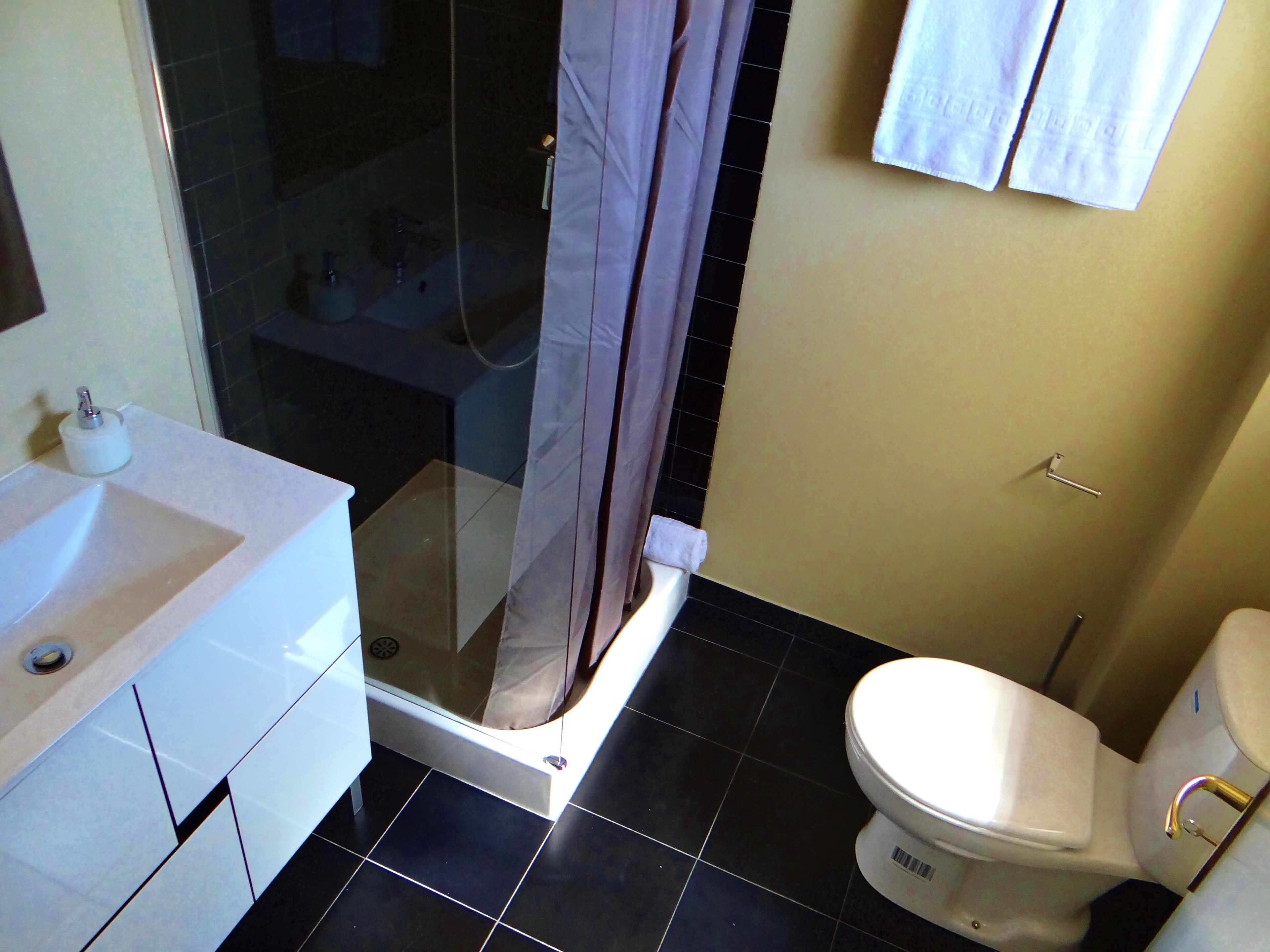 Un baño con ducha de vidrio, lavamanos blanco y retrete.