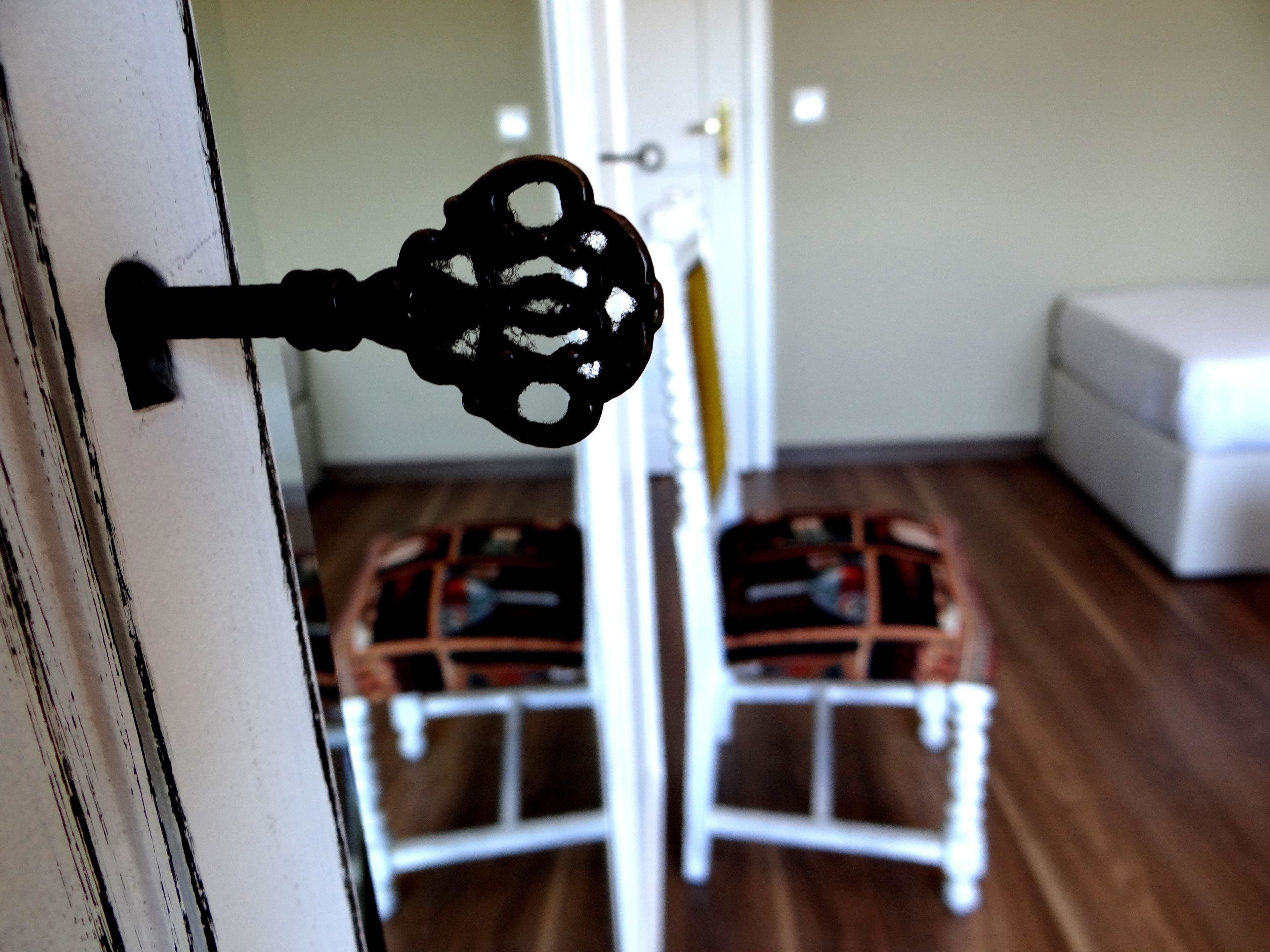 A keyhole on a white door with a wooden floor and a white chair in the background.