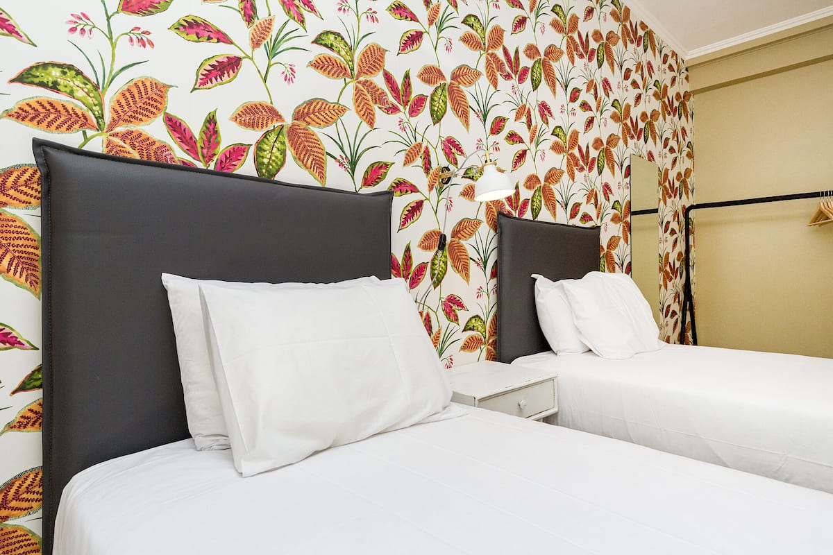 Habitación de hotel con dos camas, ropa de cama blanca y diseño de papel tapiz floral.