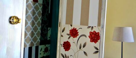 Un vano con cortina estampada, pared a rayas y una lámpara sobre una mesita de noche.