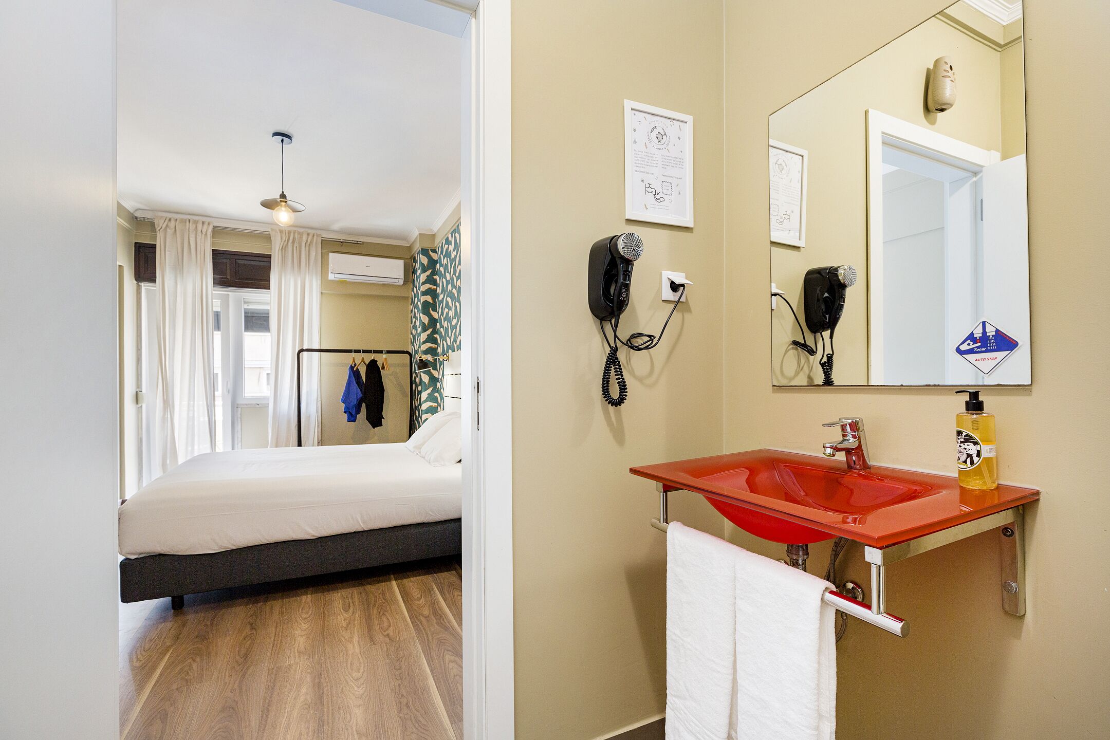 Une chambre d’hôtel avec un lit, un lavabo rouge, un miroir, un sèche-cheveux et un porte-serviettes.