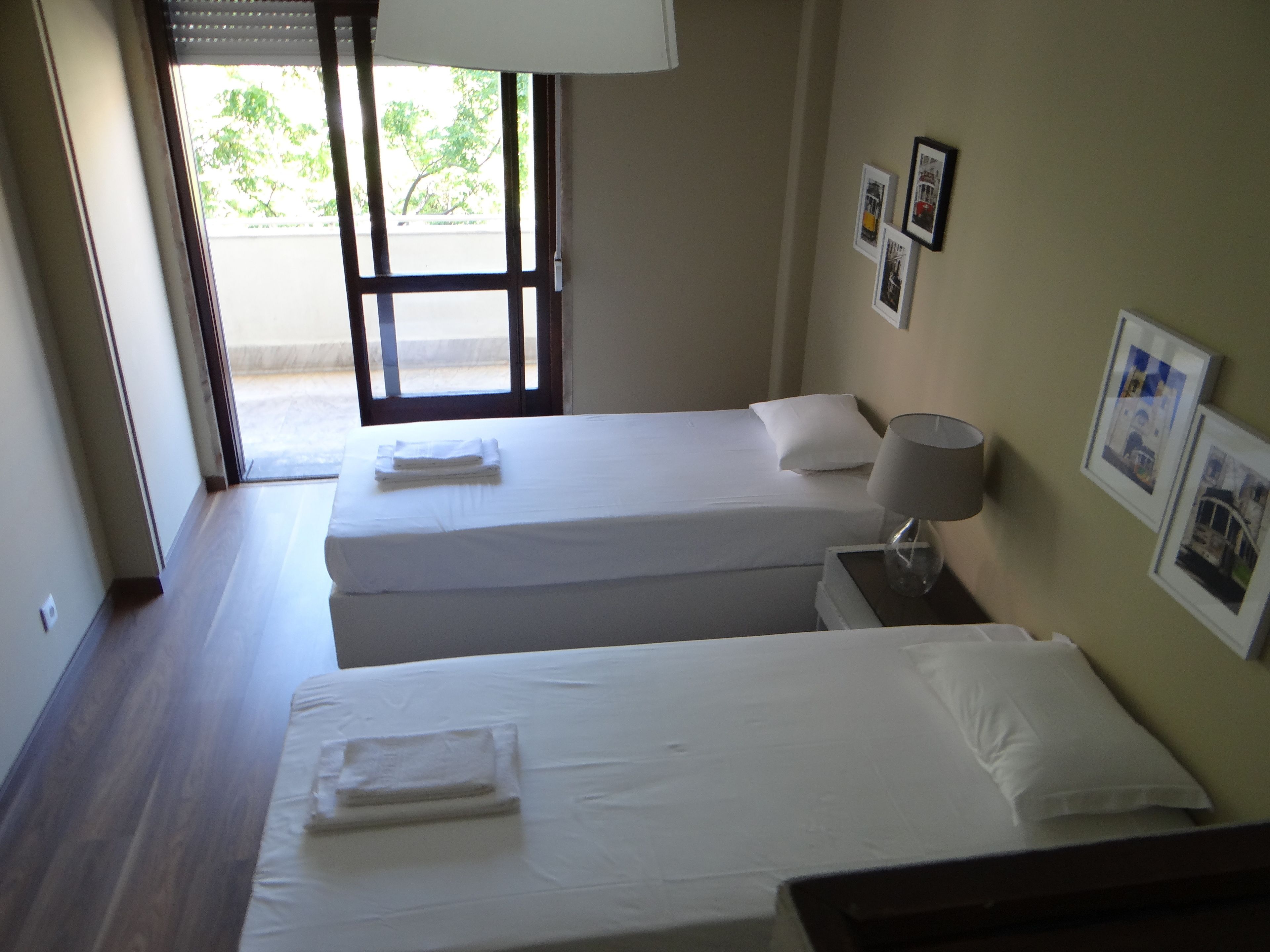 A hotel room with two beds, a nightstand, a lamp, and framed pictures on the wall.
