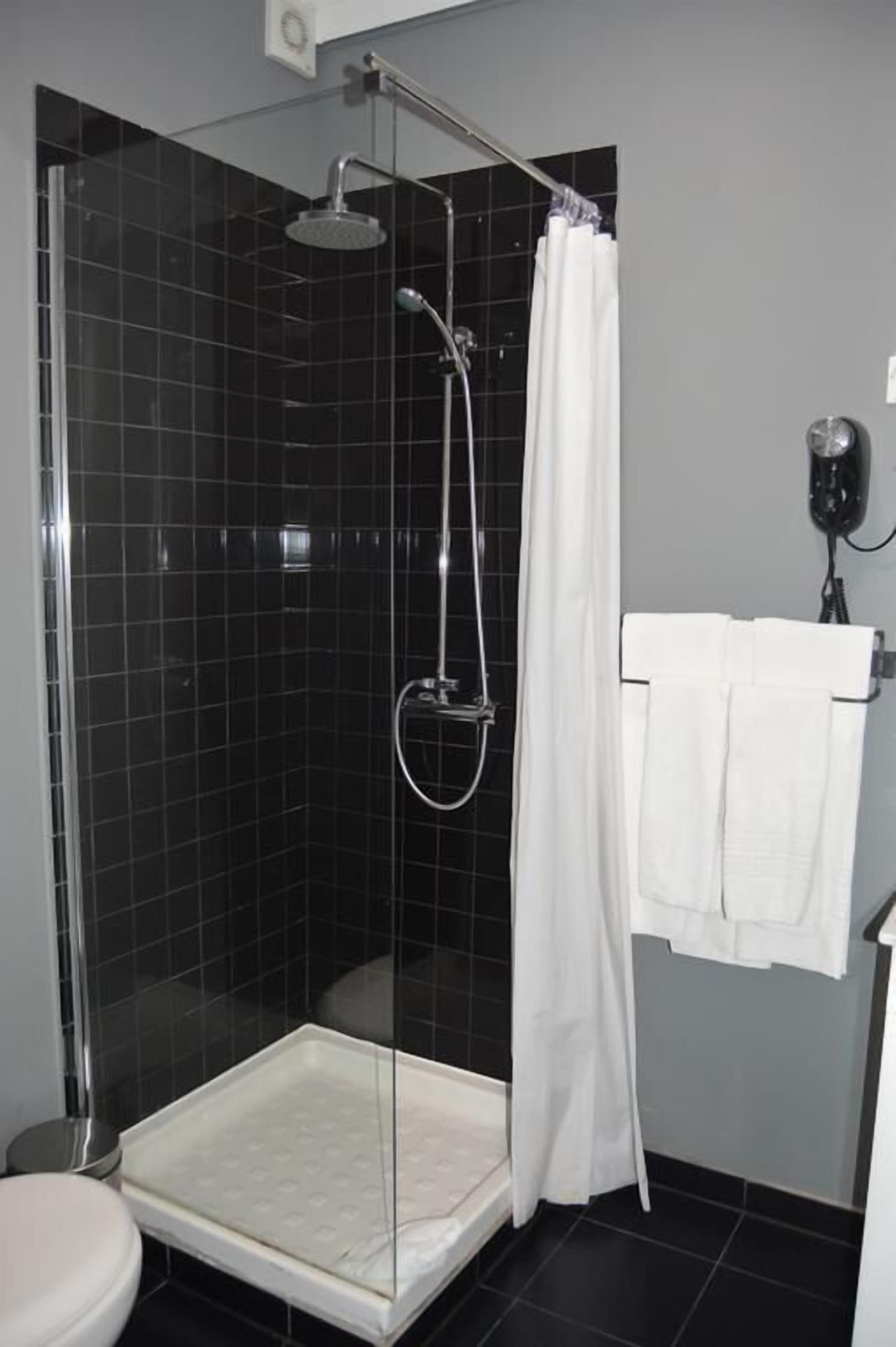 A shower with a glass door, a white towel rack, and a black tiled wall.