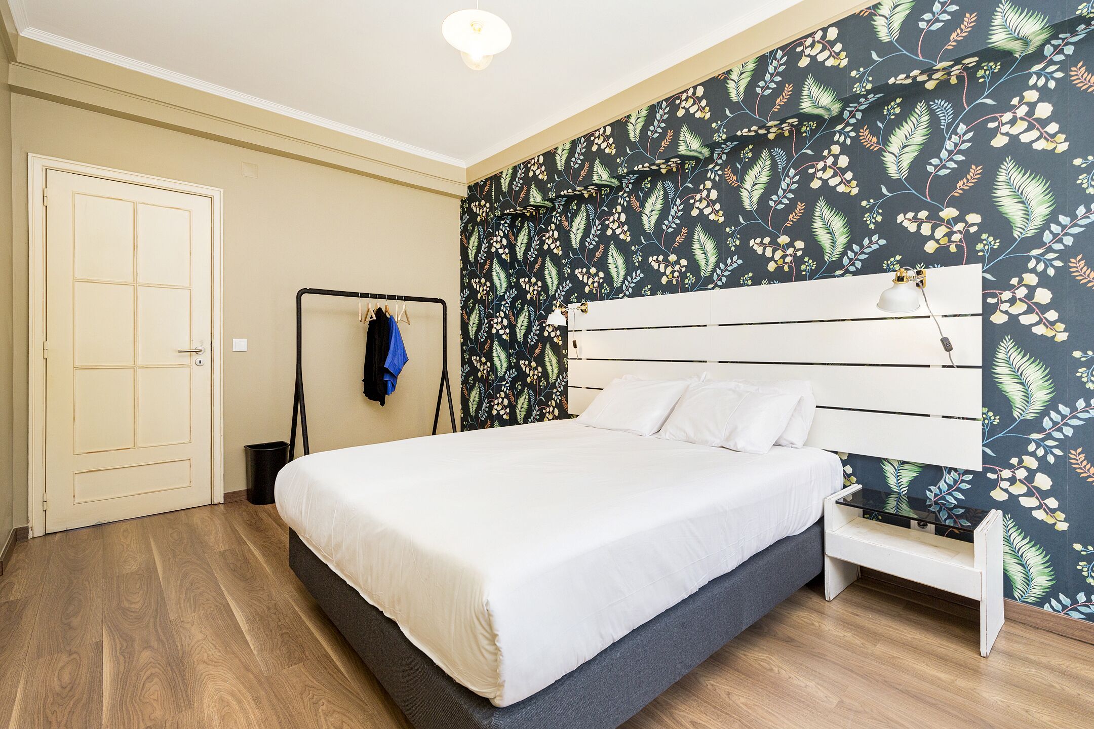 A bedroom with a bed, a wardrobe, a bench, and a wall with a leafy pattern.