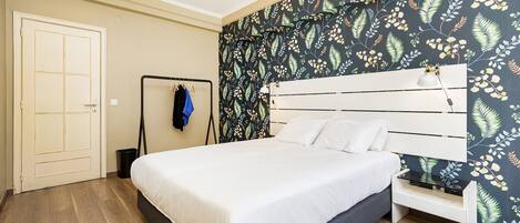 A bedroom with a bed, a wardrobe, a bench, and a wall with a leafy pattern.