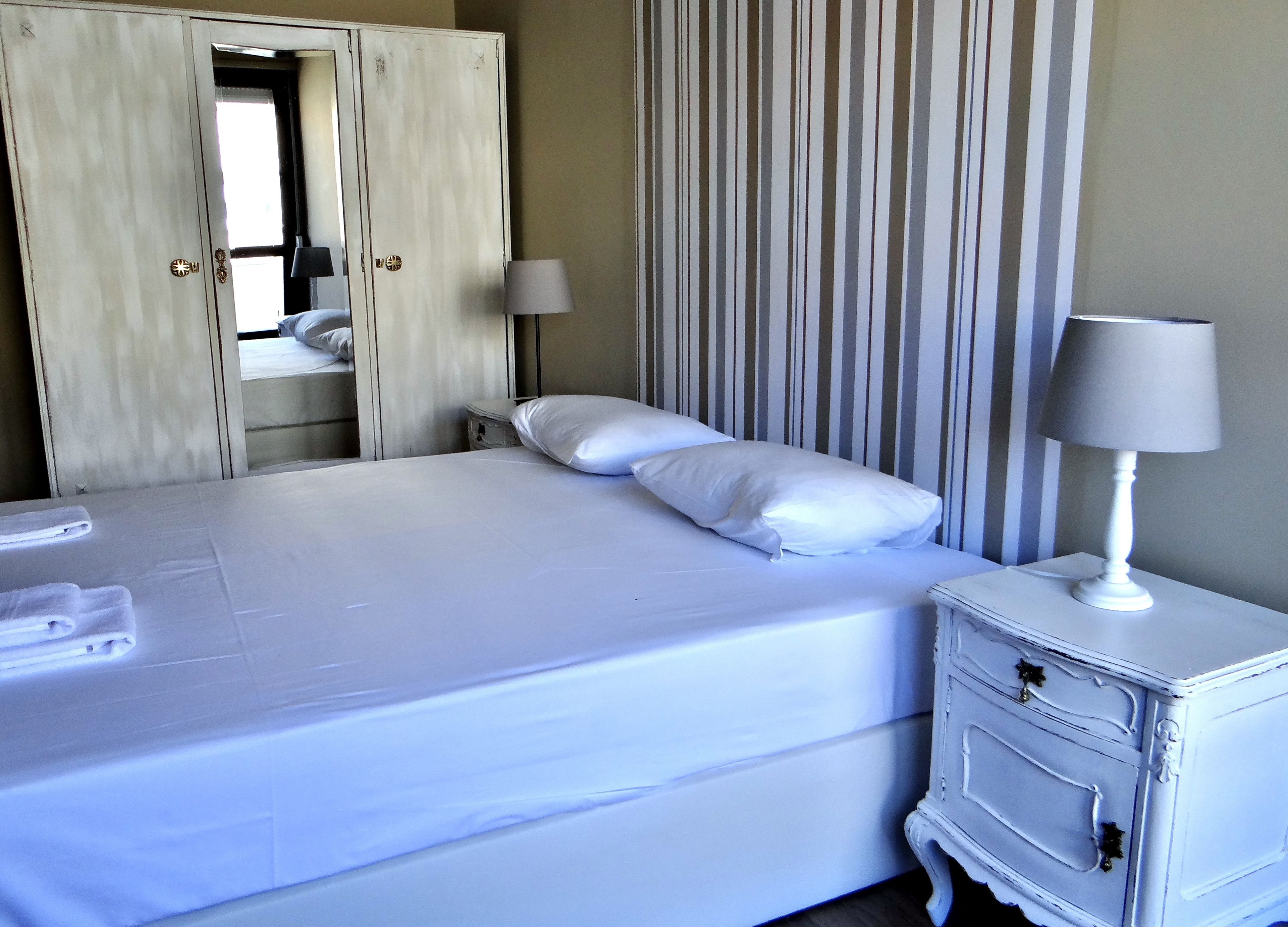 A neatly made bed with white linens, a bedside lamp, and a dresser with drawers.
