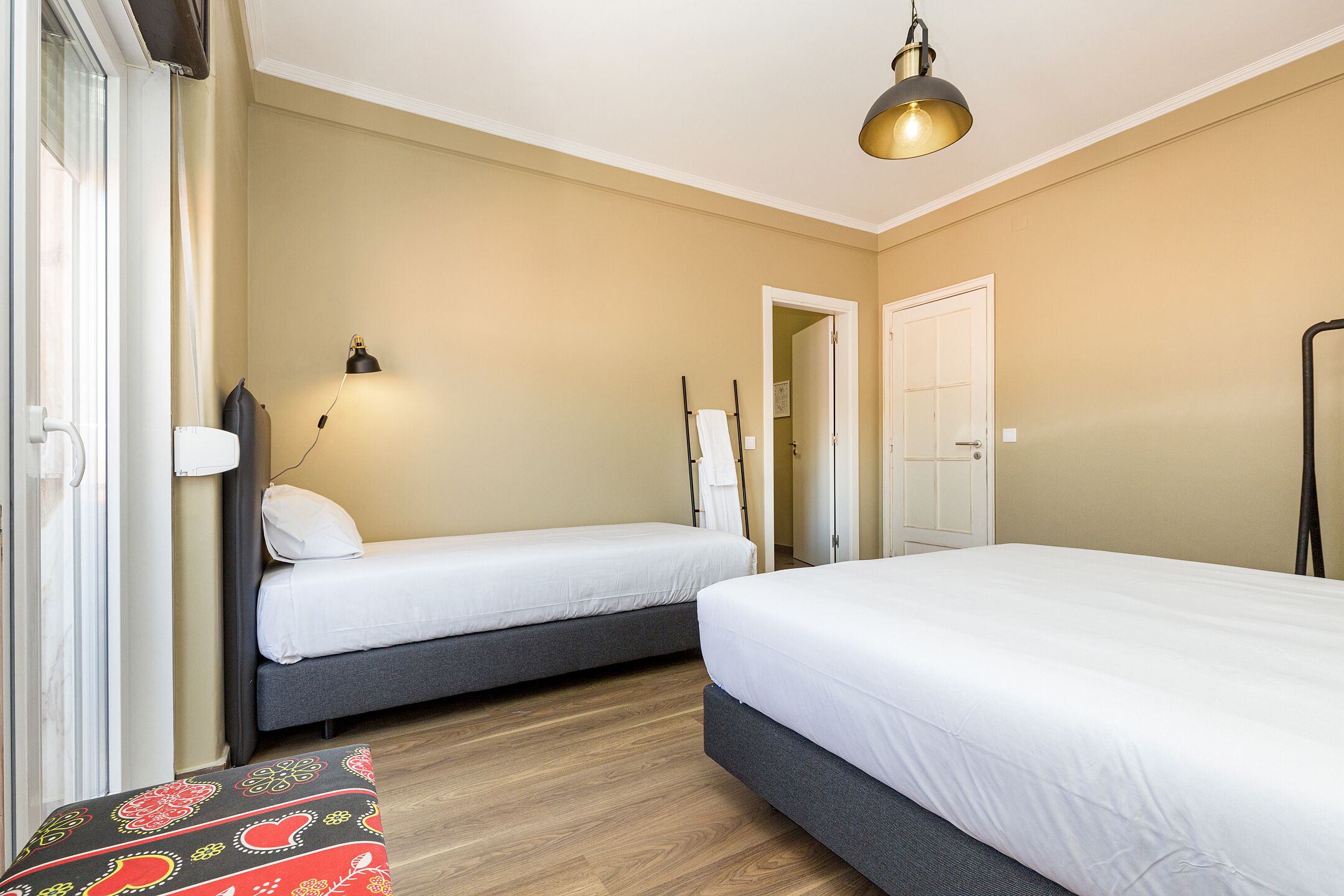 A bedroom with two single beds, a bedside table, a lamp, and a door leading to another room.